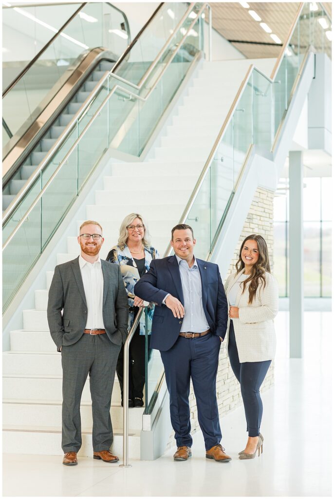 Professional team portrait of four real estate agents standing on a modern staircase in a bright, natural-lit office building, captured by Zoe Evans Photography