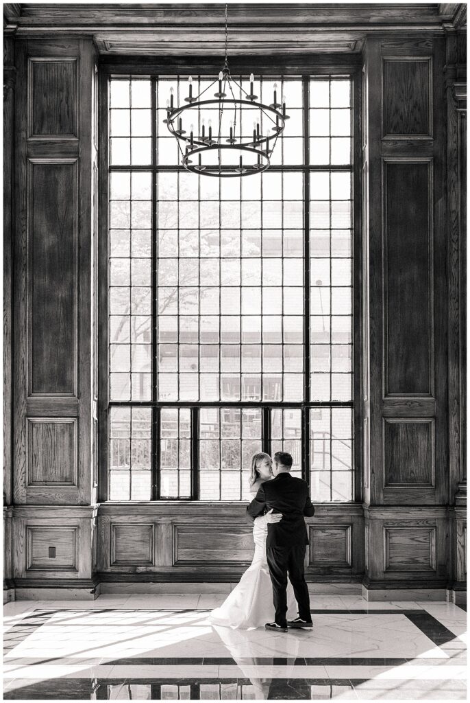 Bride and groom dancing together in front of the large, arched window at Hotel Morgan, framed by wooden paneling and soft, natural light.