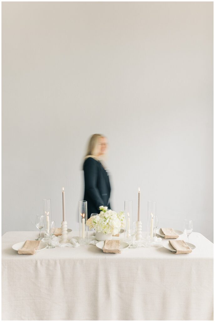 A softly blurred shot of Morgan walking past Wildflower Events neutral, chic tablescape with white florals and understated table settings, capturing a sophisticated event design style.