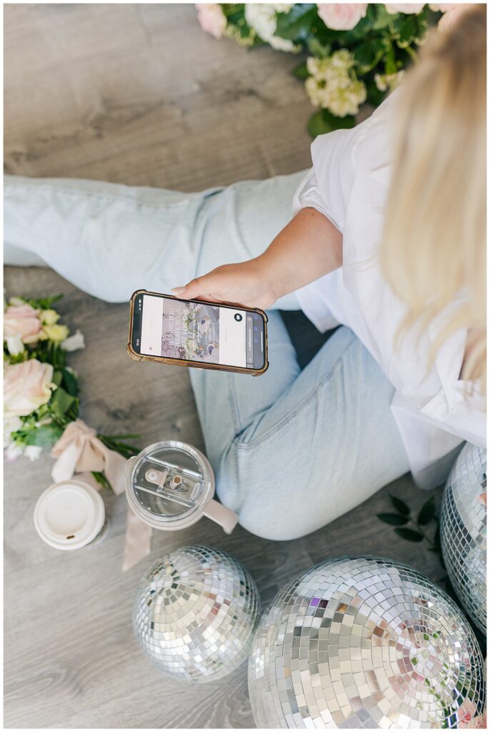 Morgan scrolling through her phone, surrounded by disco balls, flowers, and a Starbucks cup, capturing a laid-back, behind-the-scenes vibe.