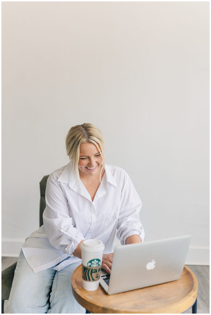 Morgan of Wildflower Events working on her laptop at 304 Collective studio, holding a coffee cup and smiling during her brand photography session.
