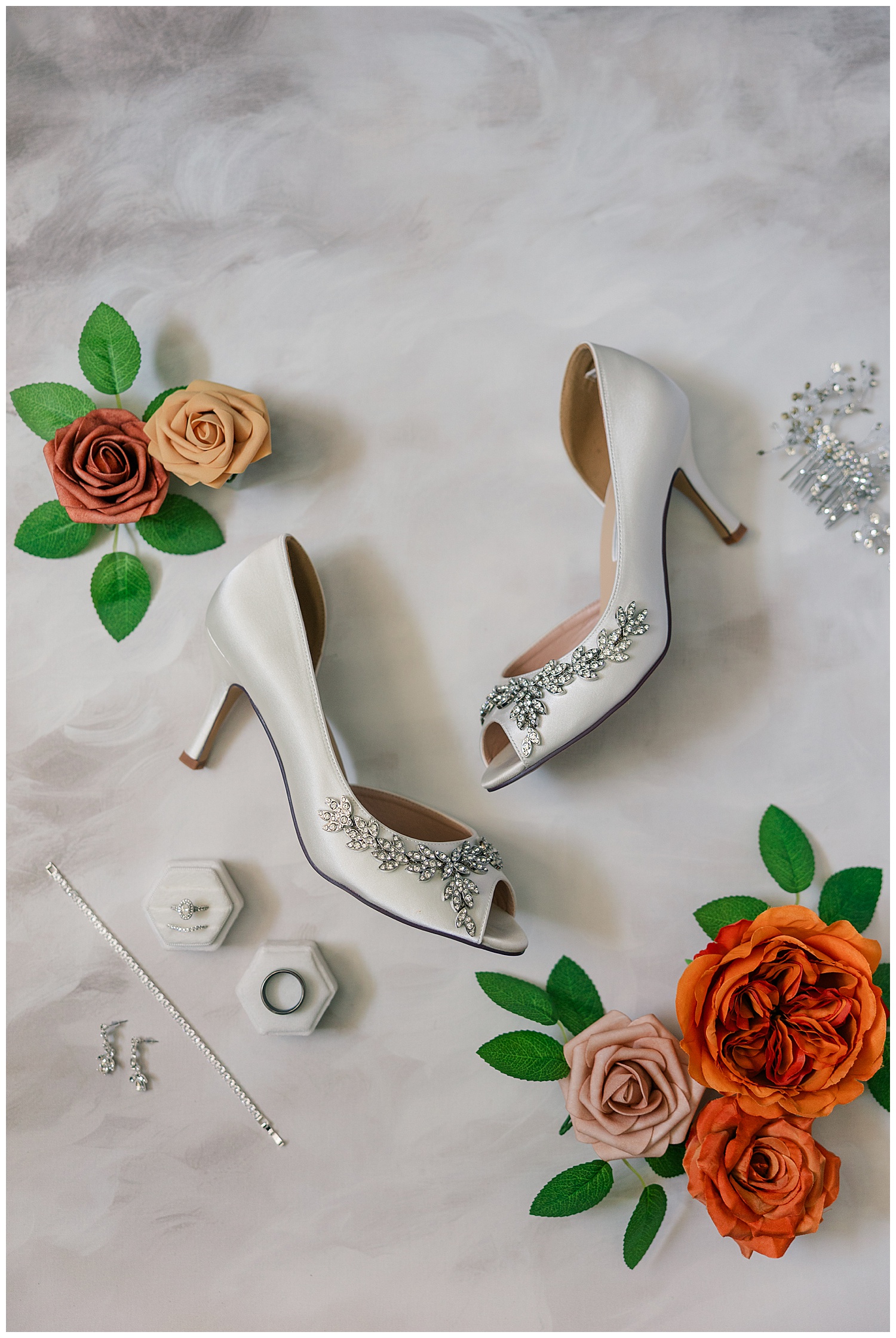 Flat lay of the bride’s shoes, jewelry, and vow books surrounded by greenery and floral accents.