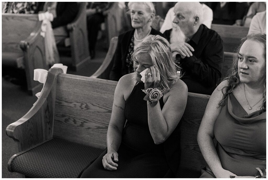 lack and white photo of a woman wiping away tears while seated in a church pew, showing an emotional moment during the ceremony.