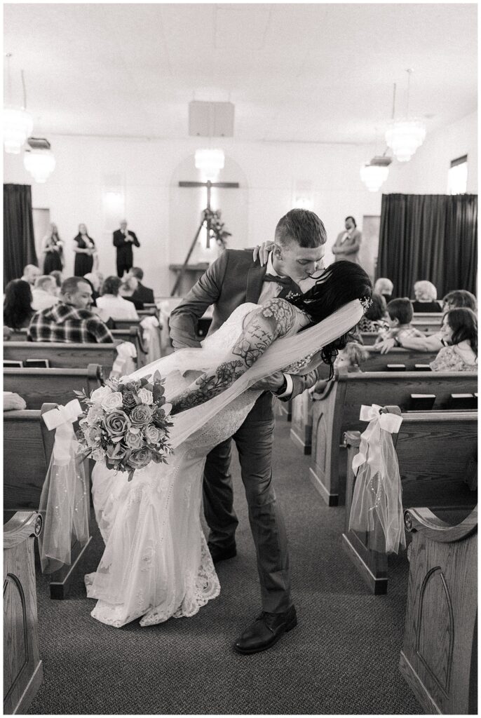 Black and white photo of the groom dipping the bride for a kiss down the aisle, just moments after being pronounced husband and wife.