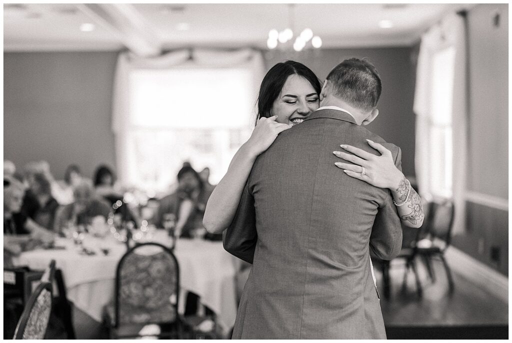 Bride and groom sharing their first dance, smiling and embracing in the center of the reception space.