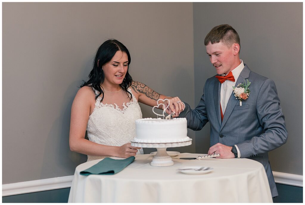 Bride and groom laughing as they cut their wedding cake together at the reception.