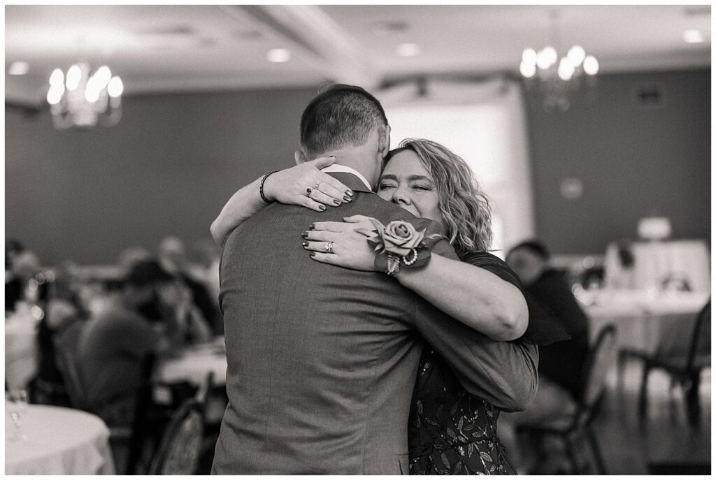 Groom hugging a mother of the groom during the wedding reception, captured in a black and white candid moment.