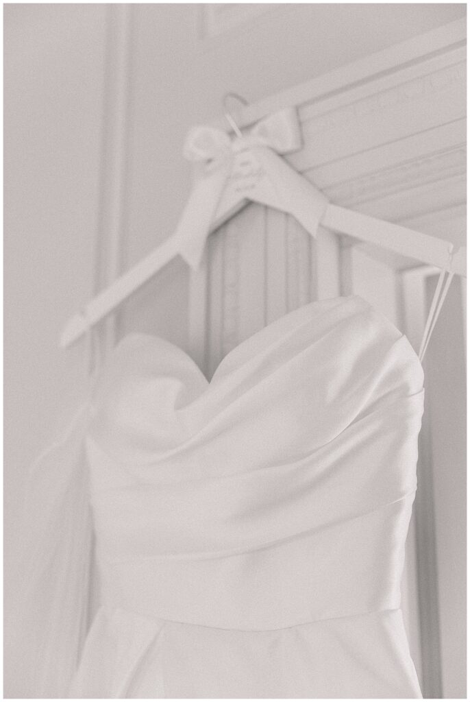 Close-up of an elegant strapless wedding gown with a sweetheart neckline, hanging on a custom white hanger with a bow detail.