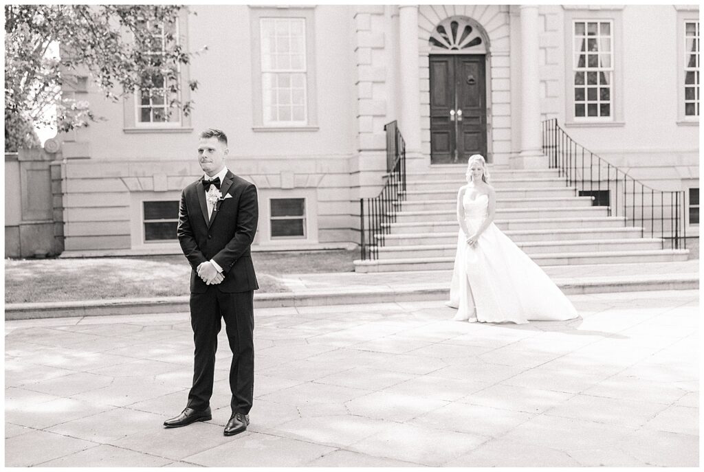 Groom waits with anticipation for the first look as the bride approaches him in her wedding gown outside the grand entrance of Great Marsh Estate.
