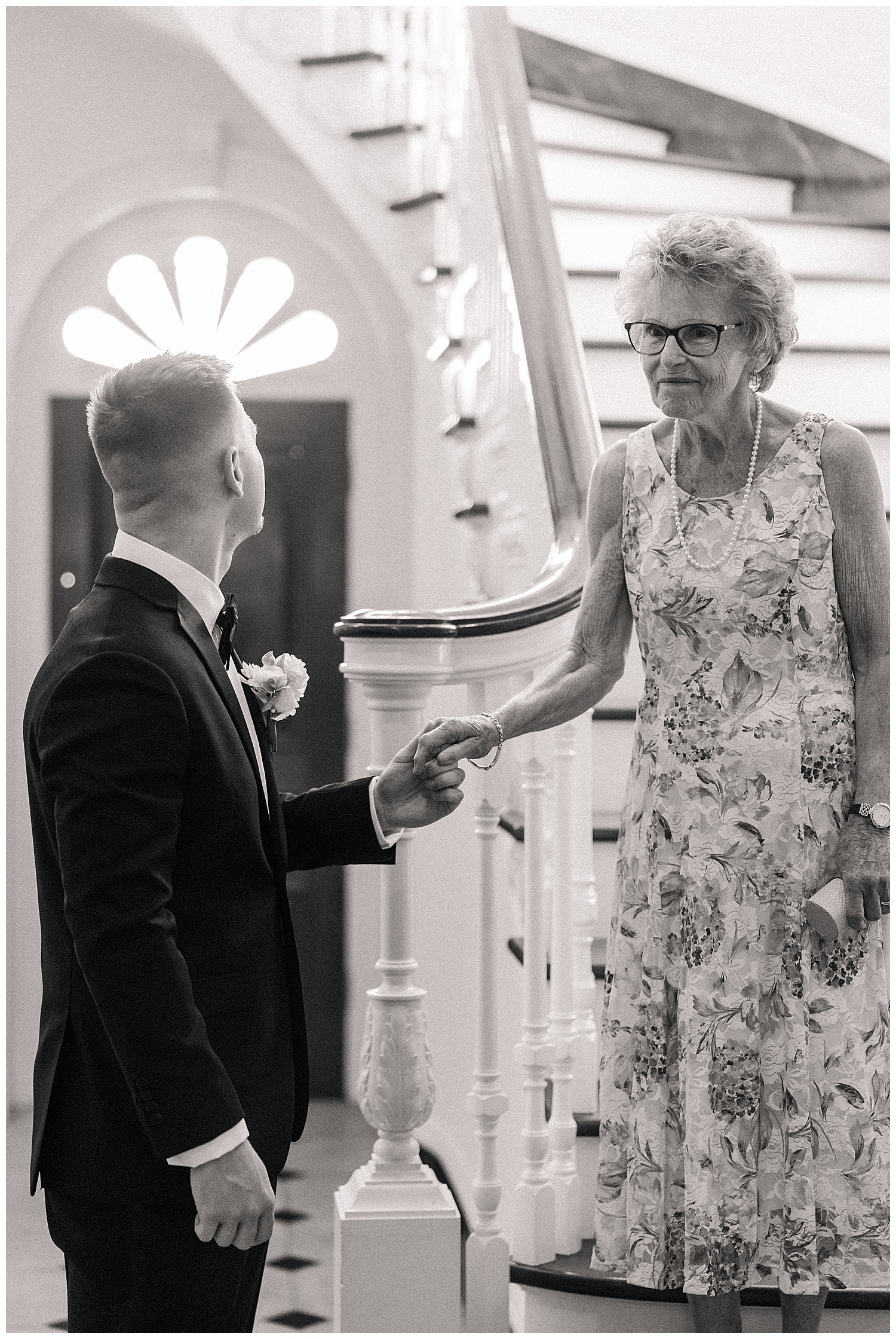 Groom warmly greets an elderly guest, gently holding her hand with a smile under an arched doorway at Great Marsh Estate.