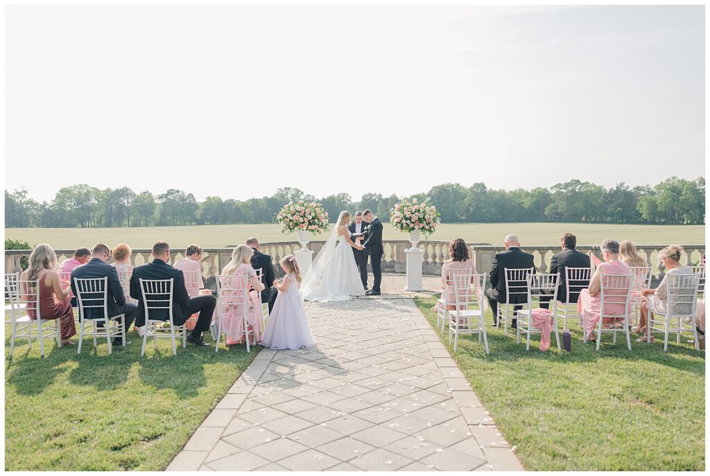 Wedding ceremony captured from behind the guests, with the couple standing at the altar surrounded by elegant florals.