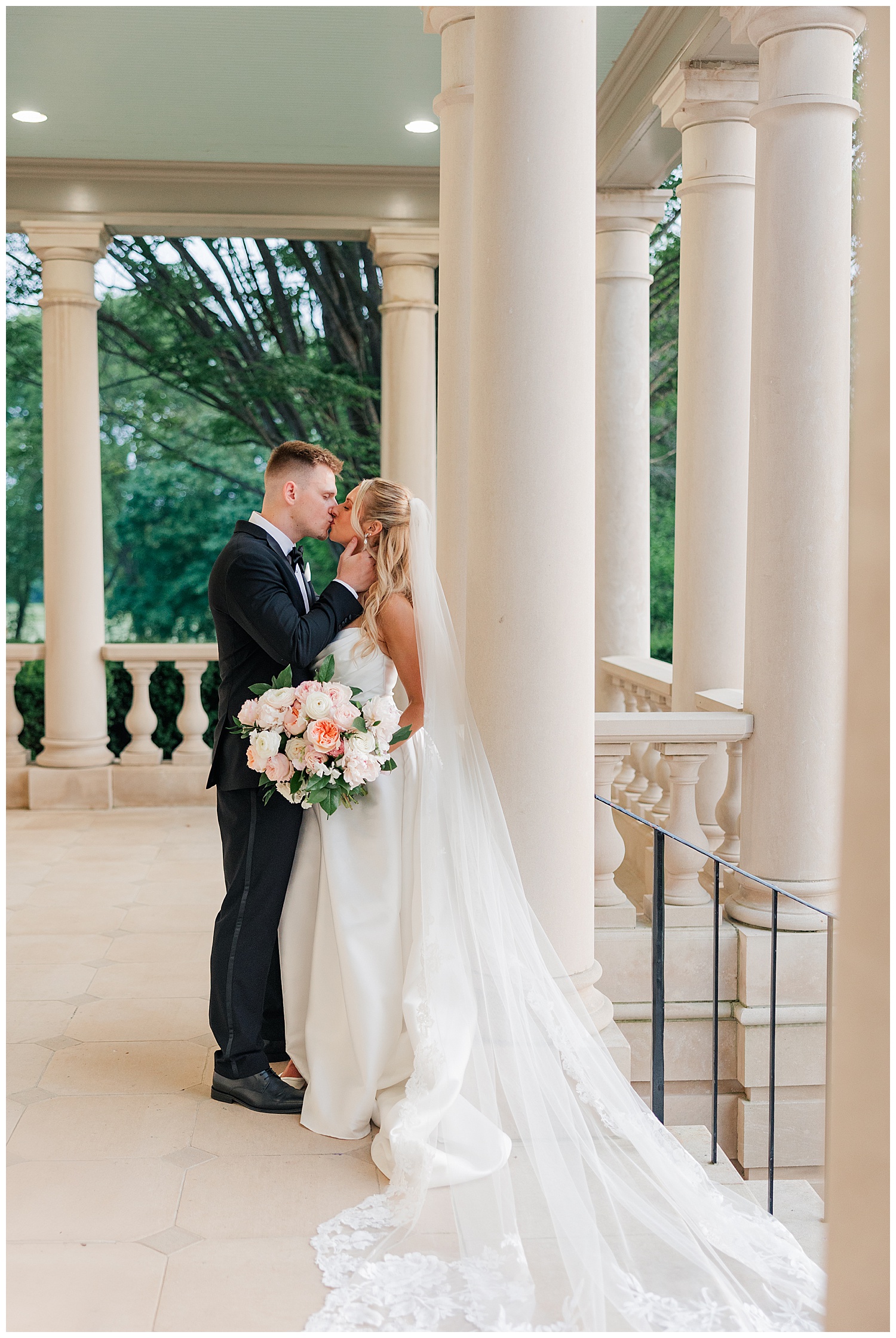 Bride and groom share an intimate moment on the columned terrace of Great Marsh Estate, the bride holding a romantic blush and white bouquet.