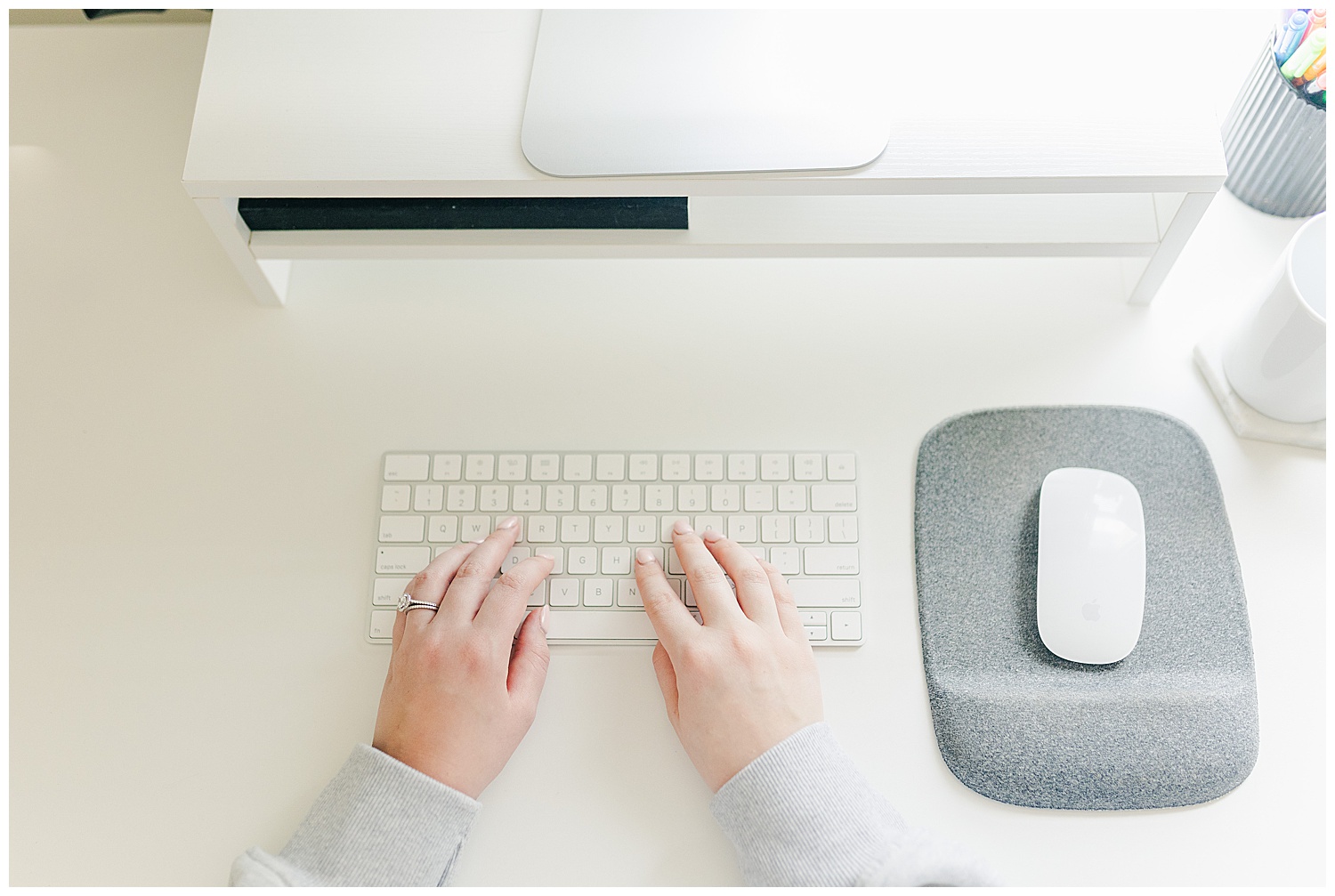 Overhead view of woman’s hands typing on a white keyboard at a minimal, clean desk setup.