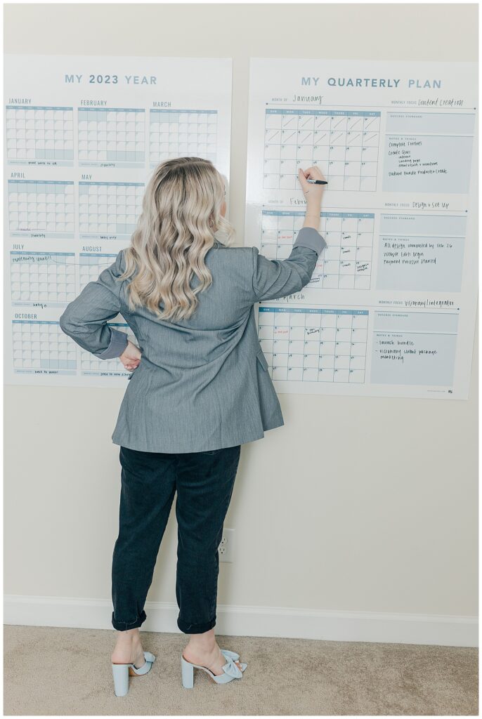 Businesswoman writing on a large wall calendar in an office, planning content or project deadlines.