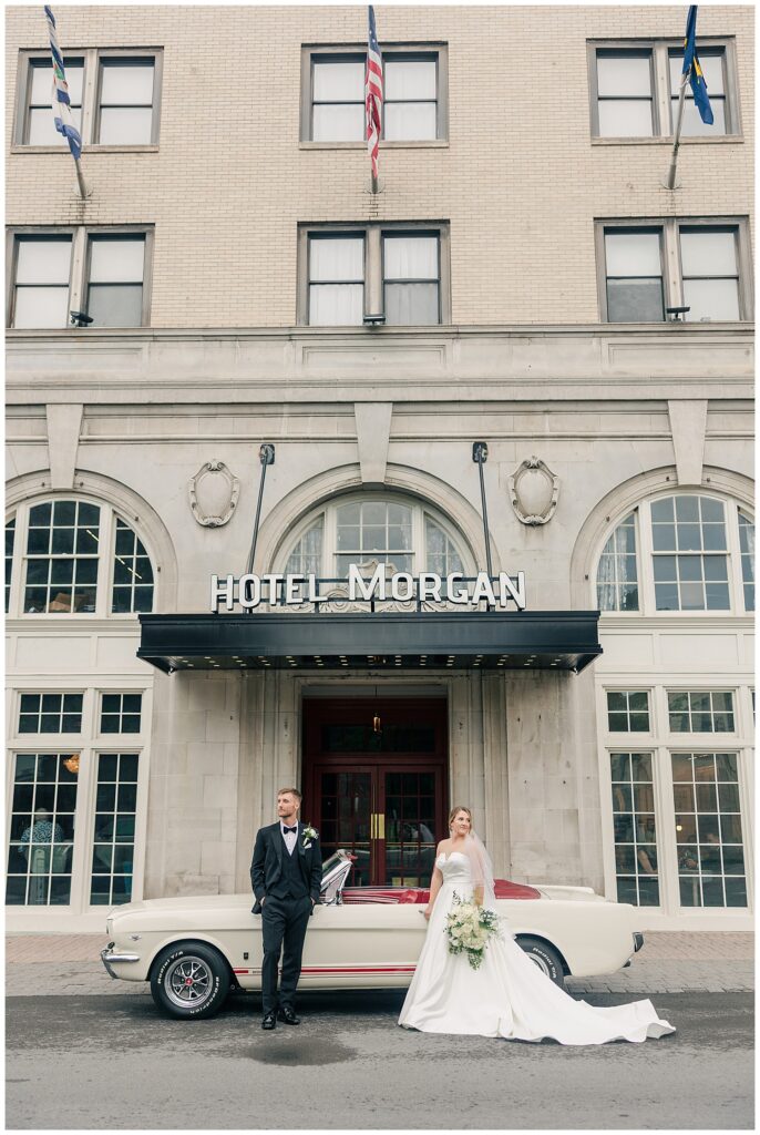 Wide-angle image of the bride and groom standing on the steps of Hotel Morgan’s grand exterior, smiling toward the camera.