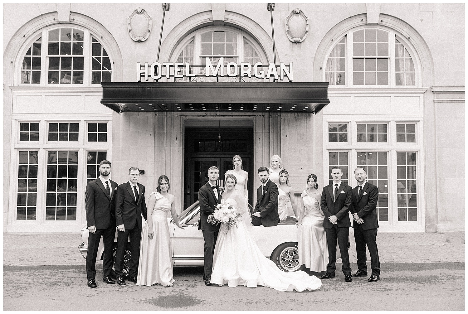 Black and white photo of the bride and groom with their wedding party standing in front of Hotel Morgan.