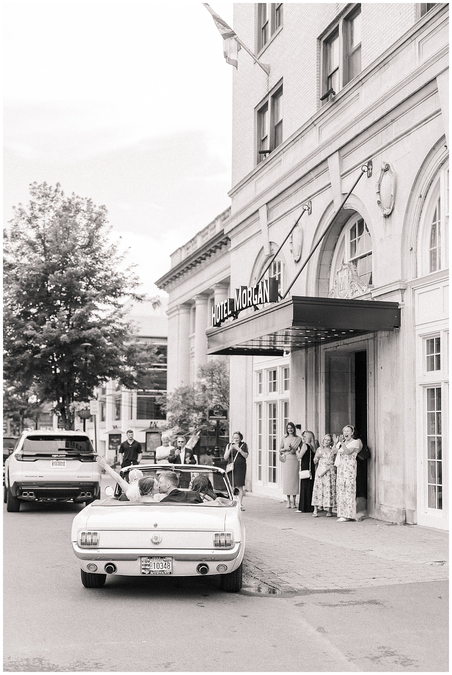 Black and white photo of the bride and groom exiting Hotel Morgan in a vintage convertible as guests wave them off.