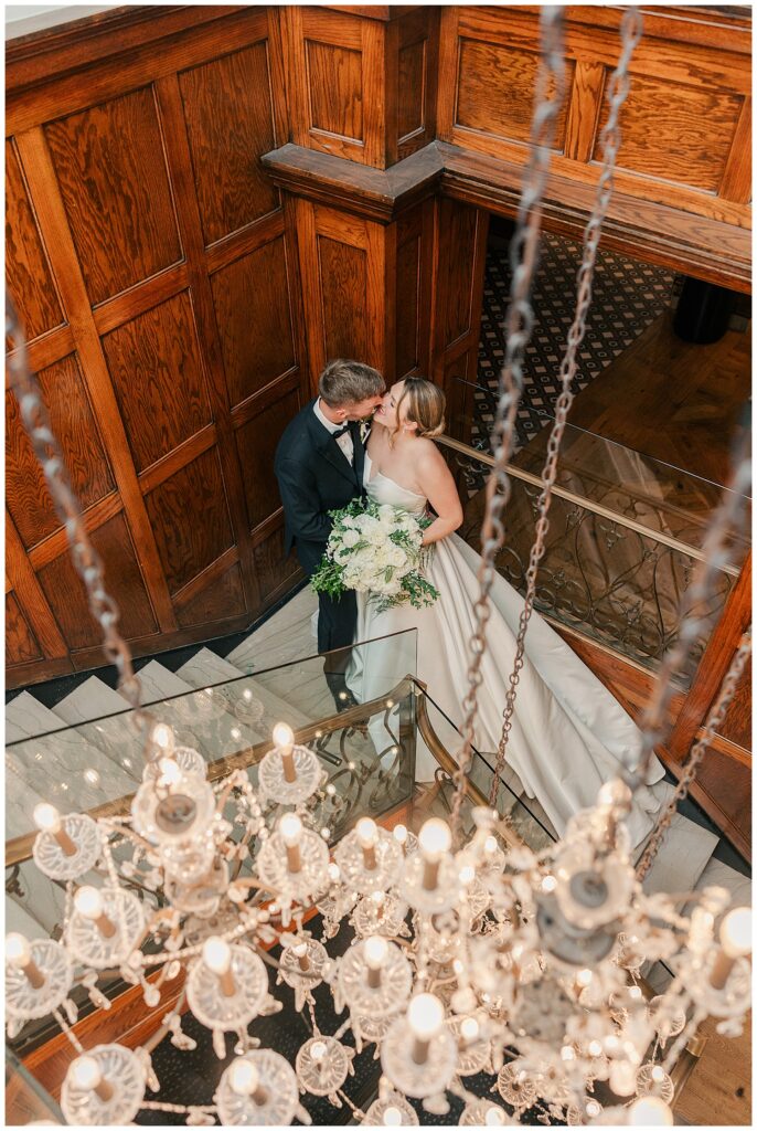 Overhead view of the bride and groom embracing on the staircase beneath a sparkling chandelier at Hotel Morgan.
