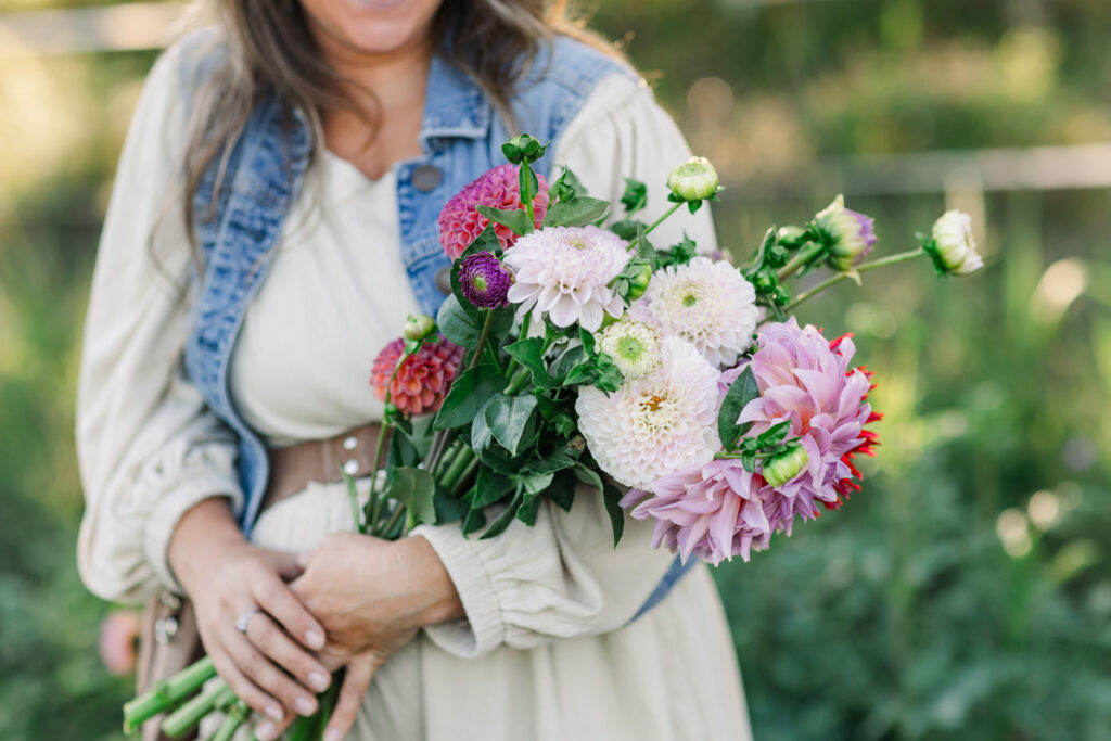 Close-up of a woman holding a vibrant bouquet of dahlias, zinnias, and white chrysanthemums
