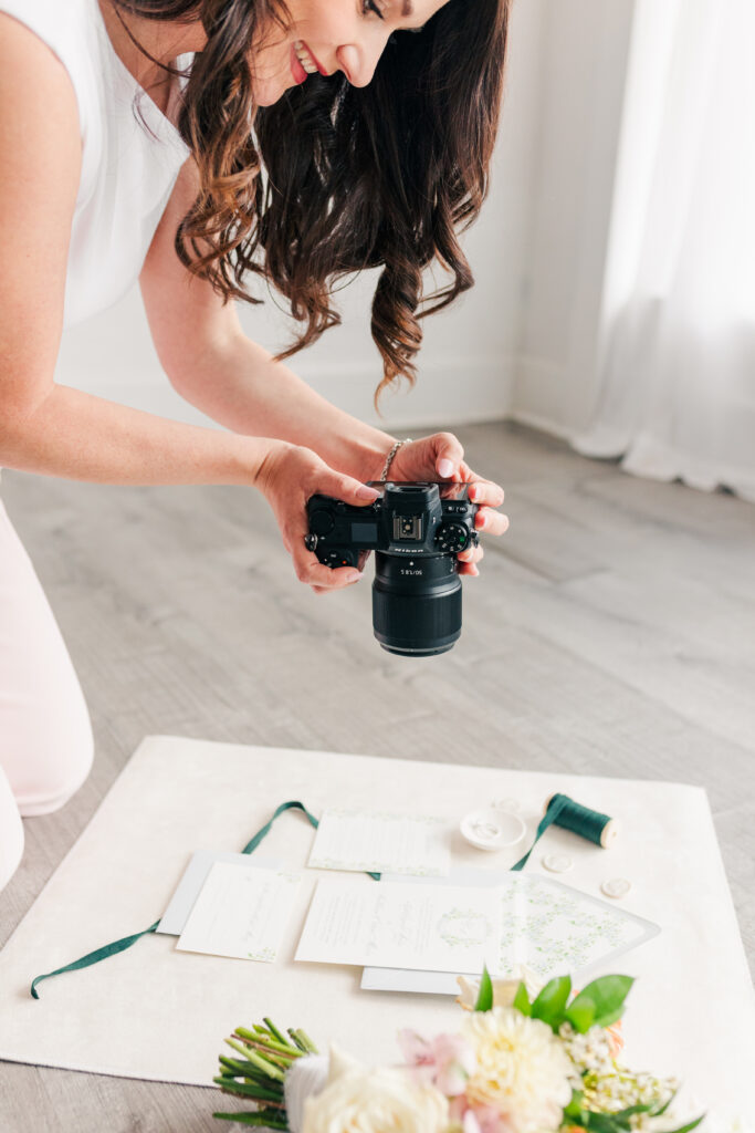 Close-up of a photographer’s hands holding a camera over styled props and flatlay setup