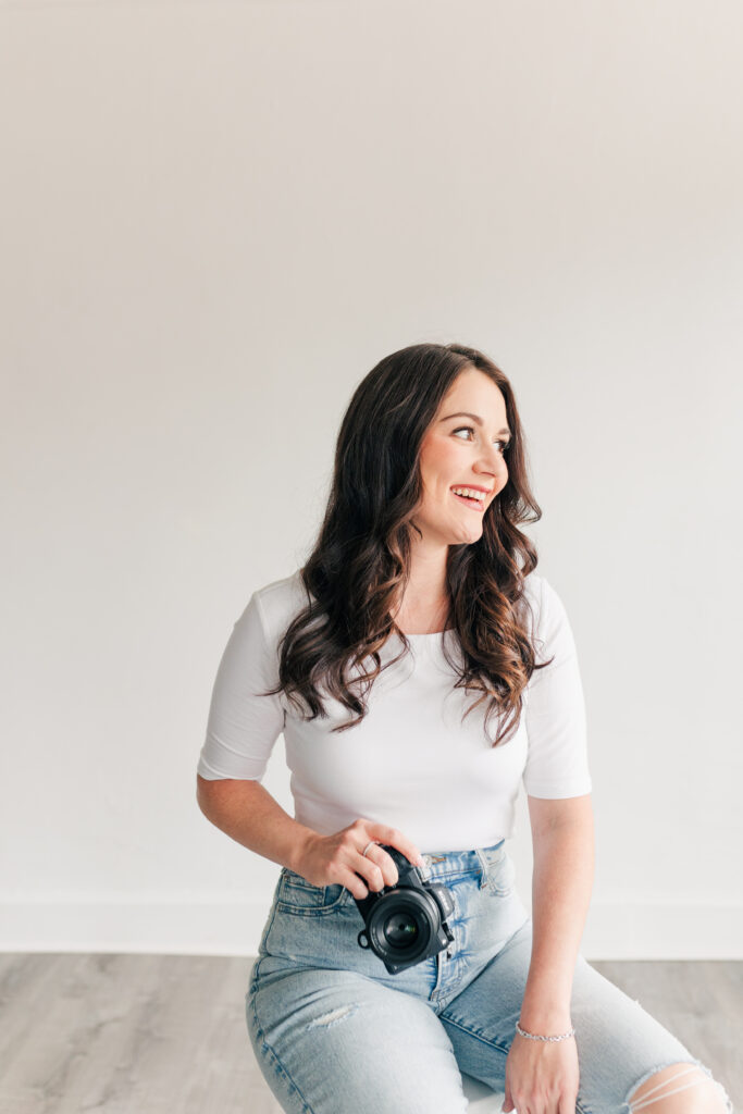Smiling woman in a white top and jeans holding a camera during brand photography session