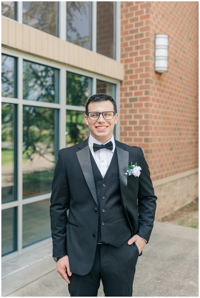 Groom portrait in tuxedo smiling in front of modern brick venue — Zoe Evans Photography
