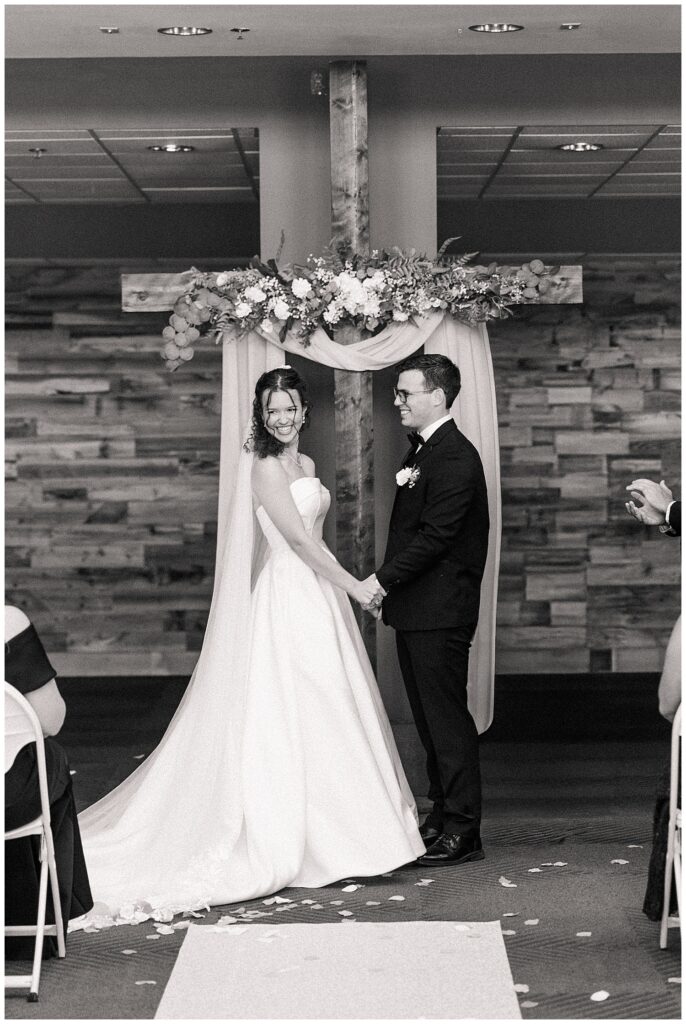 Bride and groom holding hands under floral arch during wedding ceremony — Zoe Evans Photography