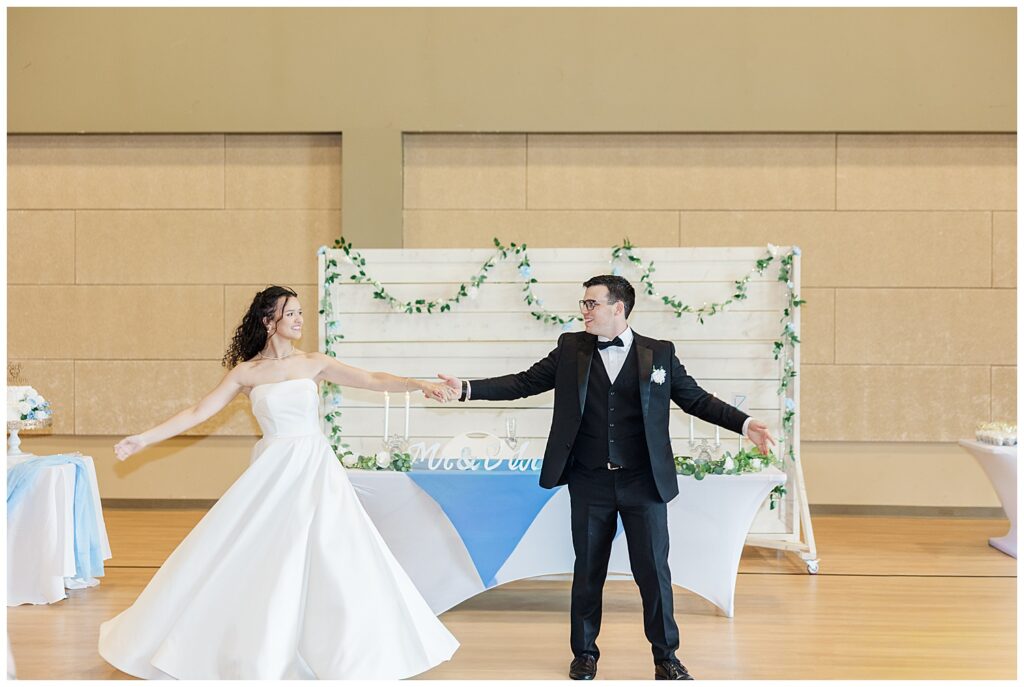 Bride and groom share a joyful spin during choreographed first dance in gymnasium venue