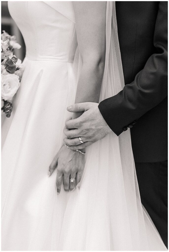 Close-up of bride and groom holding hands with bouquet in background