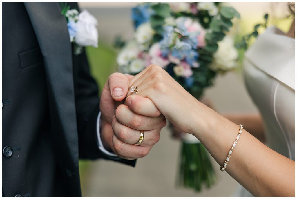 Close-up of bride and groom holding hands, with bouquet blurred in background