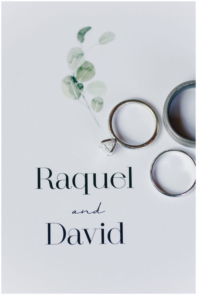 Flat lay of wedding invitation suite and rings for Raquel and David’s Red Barn Inn wedding in Deep Creek, showcasing timeless minimalist wedding details
