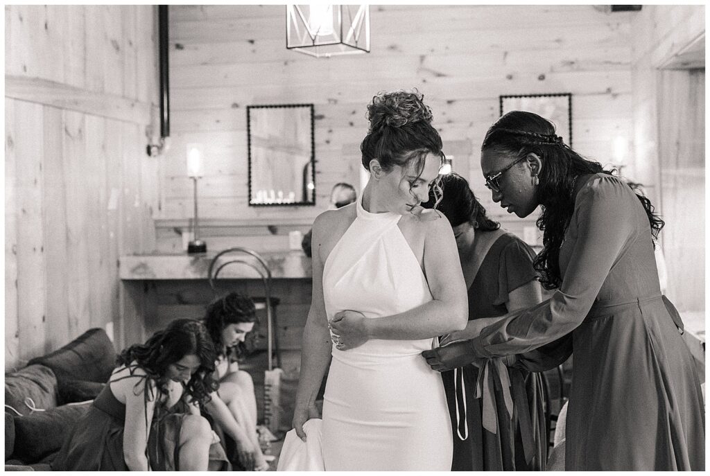 Bride getting ready with the help of her bridal party at Red Barn Inn in Deep Creek, Maryland | candid black and white wedding photo by Zoe Evans Photography