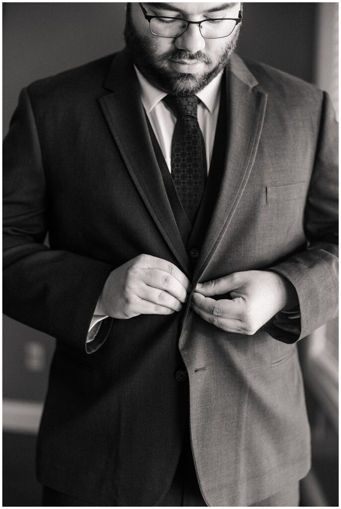 Black and white detail shot of groom buttoning his suit jacket before the wedding ceremony at Red Barn Inn | timeless groom prep captured by Zoe Evans
