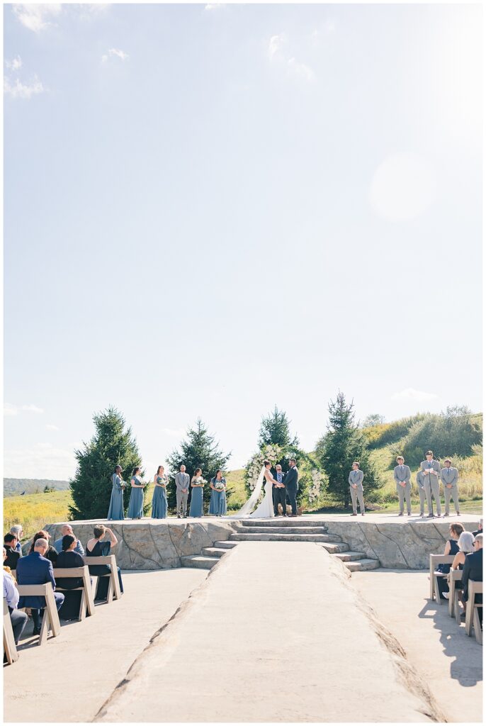 Wide angle view of outdoor ceremony with stone steps, wedding party, and scenic greenery at Red Barn Inn in Deep Creek