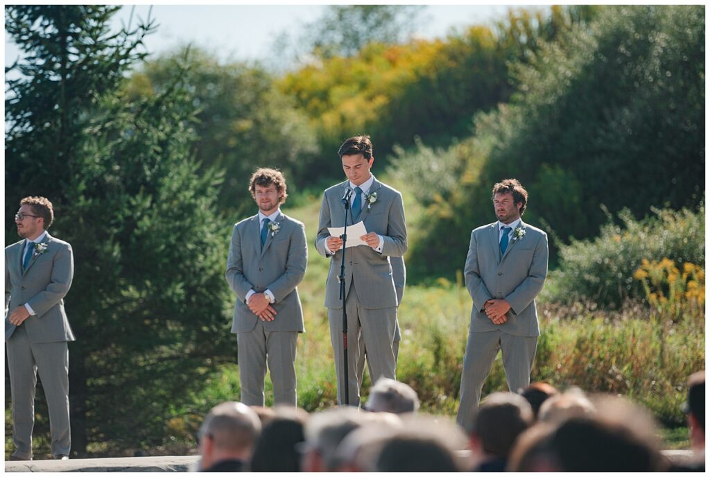 Groomsmen delivering a heartfelt bilingual speech during outdoor wedding ceremony with rolling hills backdrop