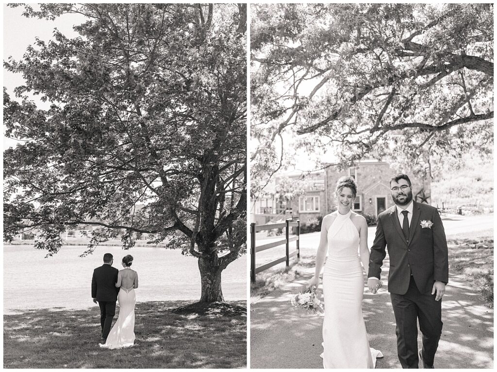 Black and white photo of newlyweds walking hand in hand beneath a large tree by the lake at Red Barn Inn