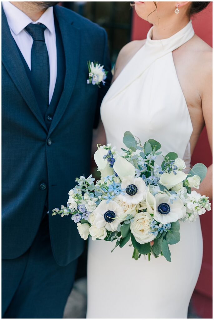 Close-up detail of white floral bouquet with blue accents held between bride and groom in formal wedding attire