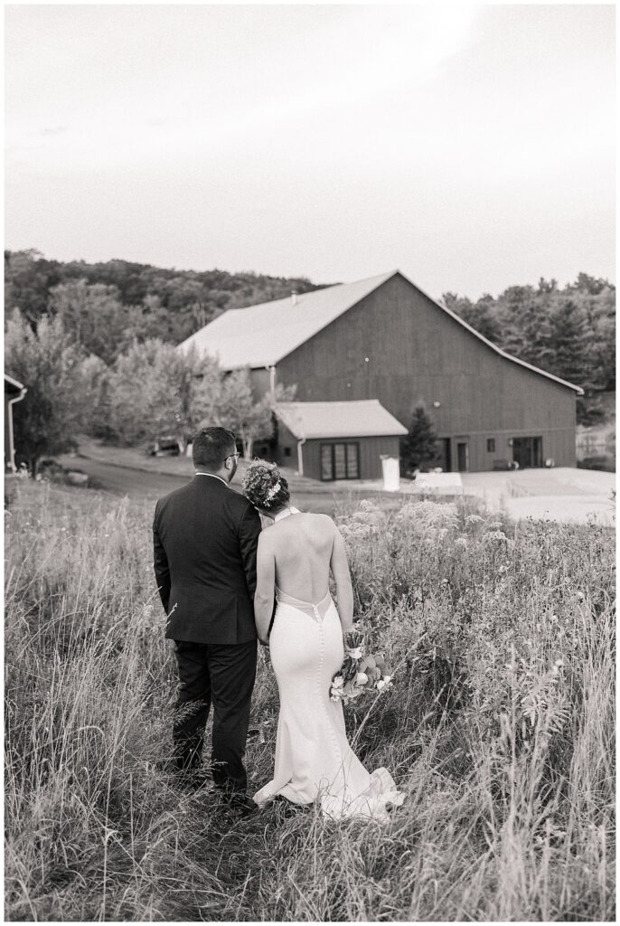 Black and white photo of couple walking toward Red Barn Inn, captured from behind through tall grass