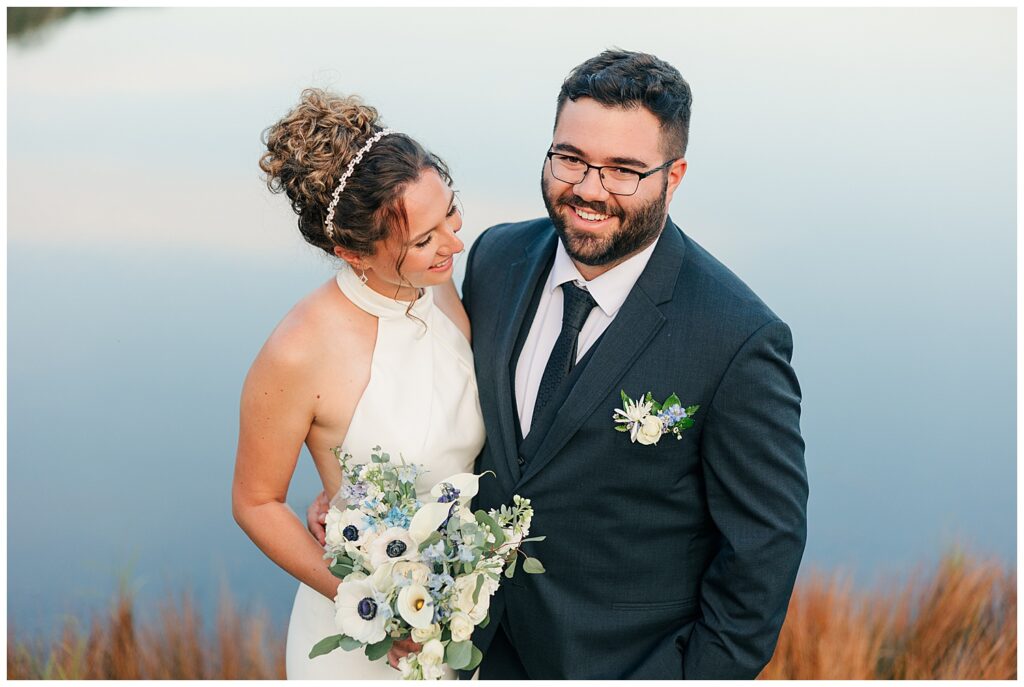 Bride and groom smiling together during golden hour portraits, bride holding white and blue floral bouquet