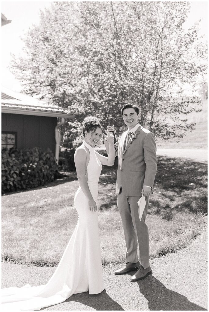 Black and white photo of the bride sharing a laugh with a groomsman outside on the lawn