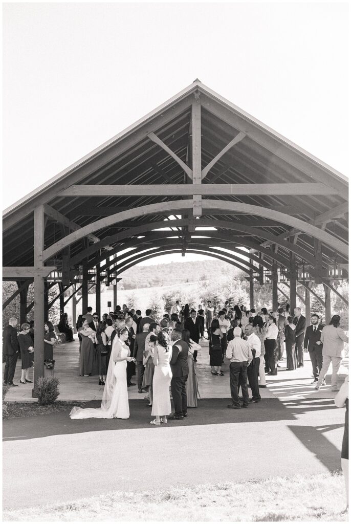 Black and white candid of guests mingling during cocktail hour under the open-air pavilion at Red Barn Inn
