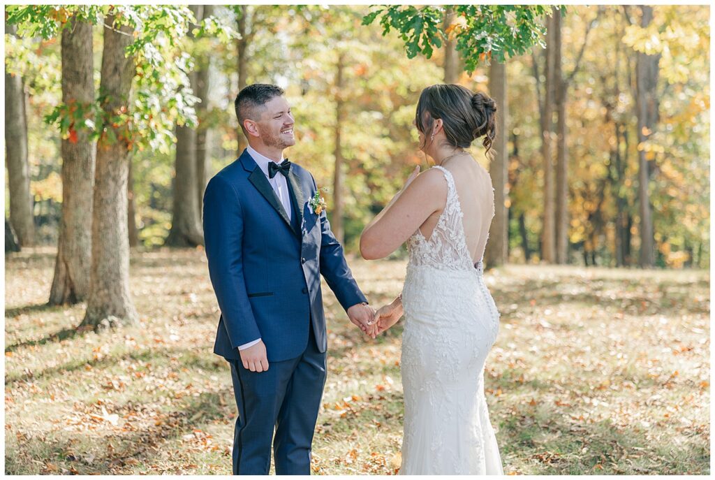 Bride and groom holding hands during emotional outdoor first look surrounded by fall foliage.