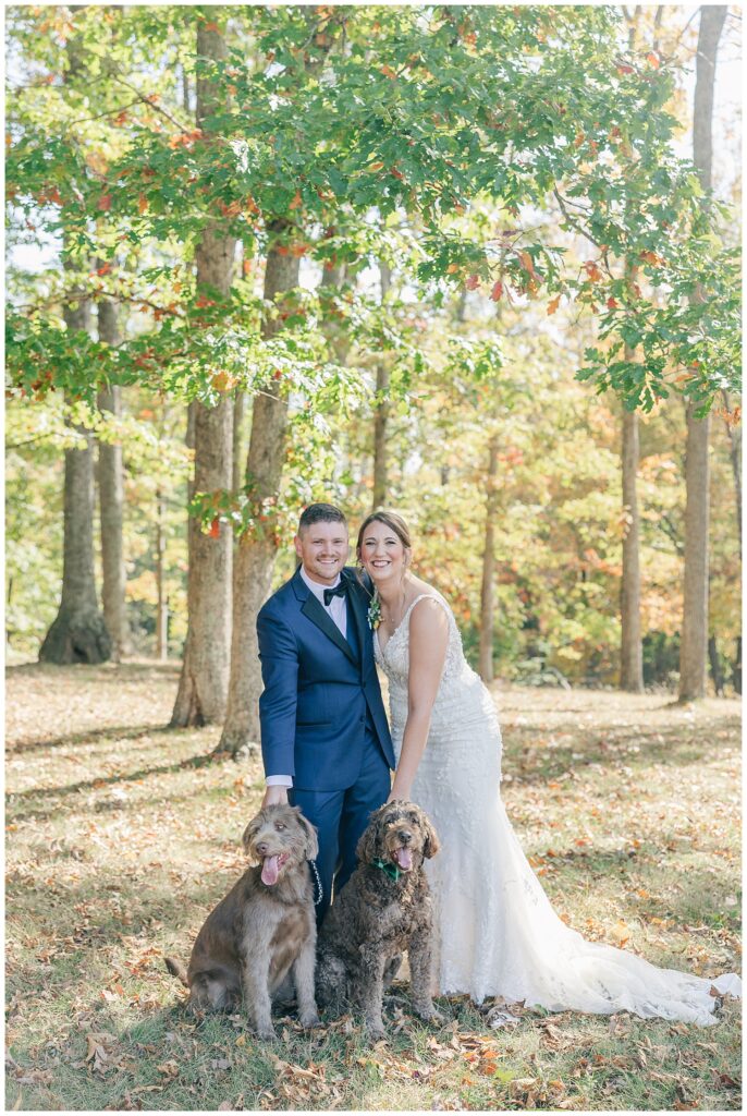 Bride and groom posing with their two dogs in the woods surrounded by autumn leaves at Athena Estate & Vineyard