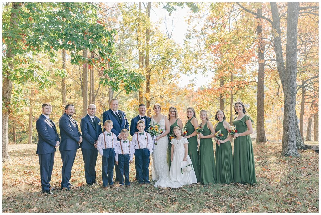 Full wedding party standing together in a wooded ceremony spot during fall at Athena Estate & Vineyard
