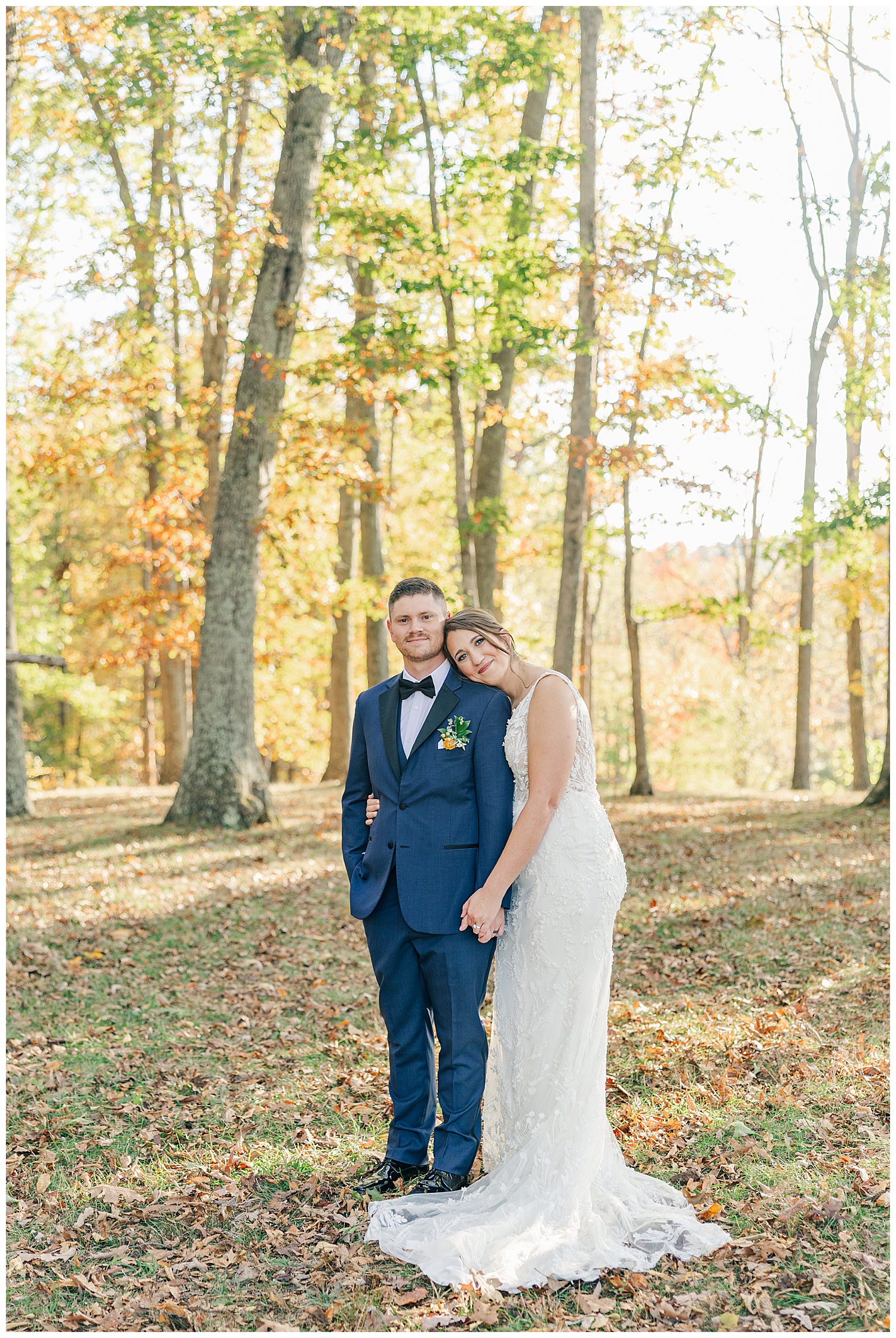 Bride and groom standing together in a wooded area during golden hour with vibrant fall foliage in the background.