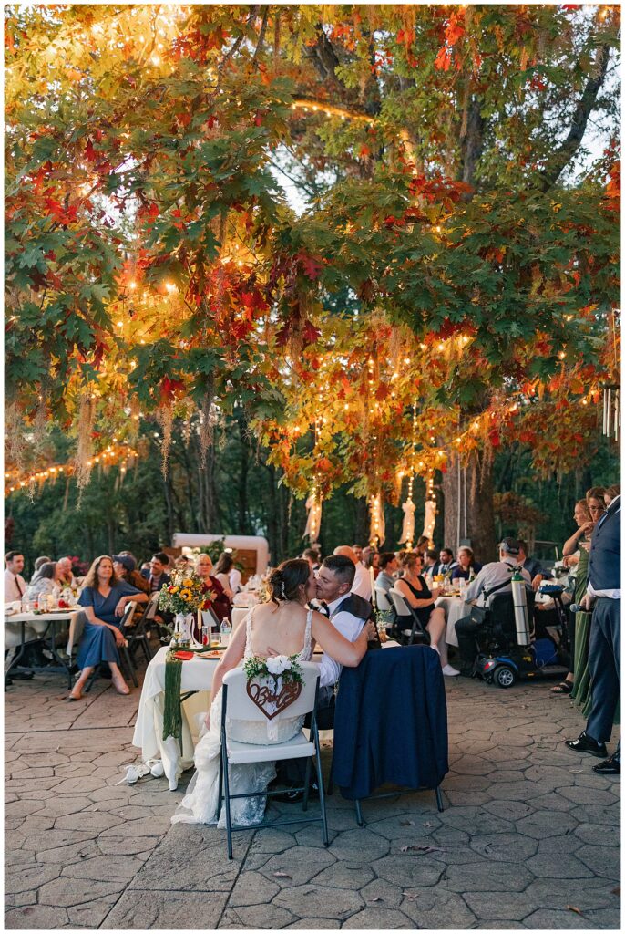 Another angle of guests seated beneath a dreamy canopy of colorful fall leaves and evening string lights.