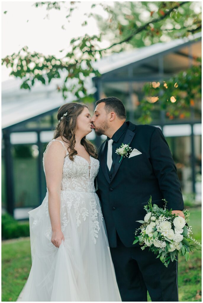 Bride and groom smiling at each other during their Ellis House reception, Newlywed kiss outside glass-paneled reception space at Ellis House Maryland, by Zoe Evans Photography.