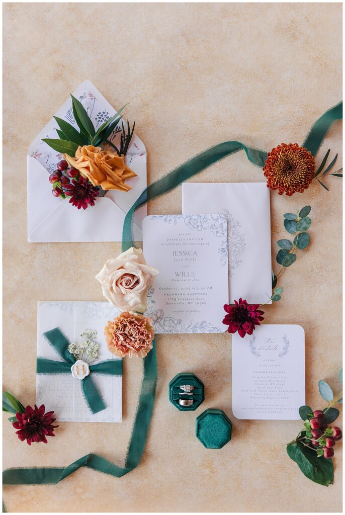 Fall wedding flat lay featuring emerald vow books, floral accents, and wedding bands at Palomino Pastures in Ritchie County, WV.