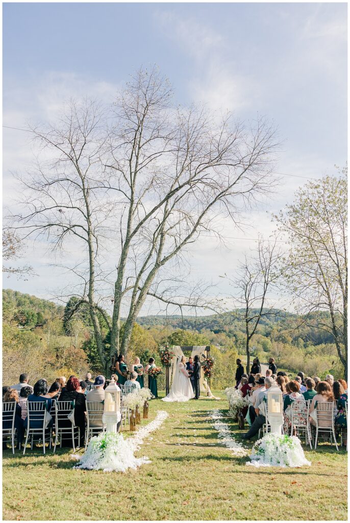 Bride and groom standing at the altar surrounded by guests seated on either side of the outdoor aisle at Palomino Pastures.