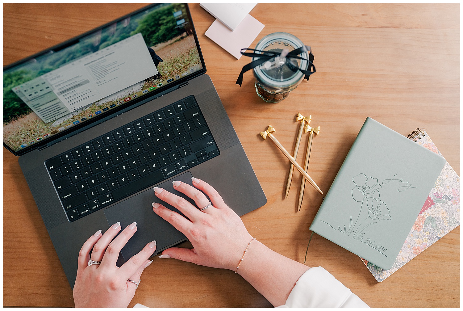 Flat lay of a laptop with a woman typing, surrounded by coffee, gold pens, and a notebook, representing productivity and remote work vibes.